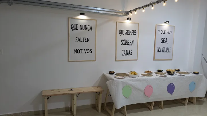 Mesa decorada con globos, banco de madera y cuadros bajo una guirnalda de luces.