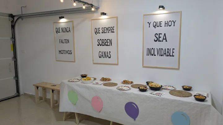 Mesa de celebración con mantel blanco, aperitivos y decoración de globos de colores.